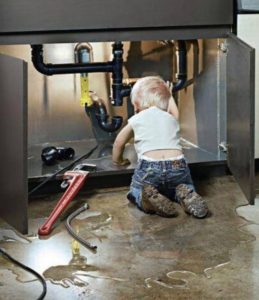 Child exploring under a sink with plumbing pipes, surrounded by water, emphasizing the importance of hiring professional plumbers to avoid DIY mishaps.